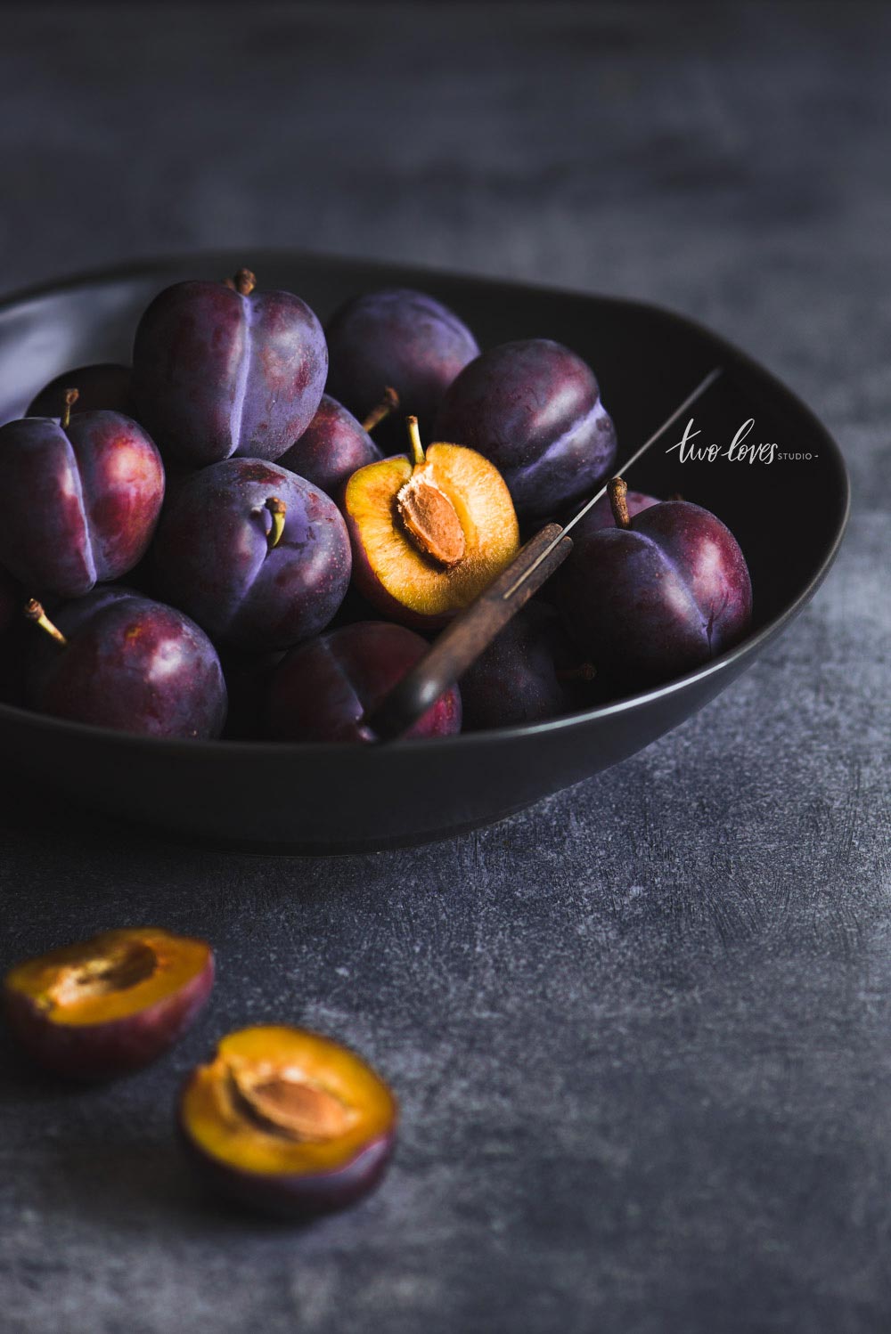 A bowl of plums with one cut in half.