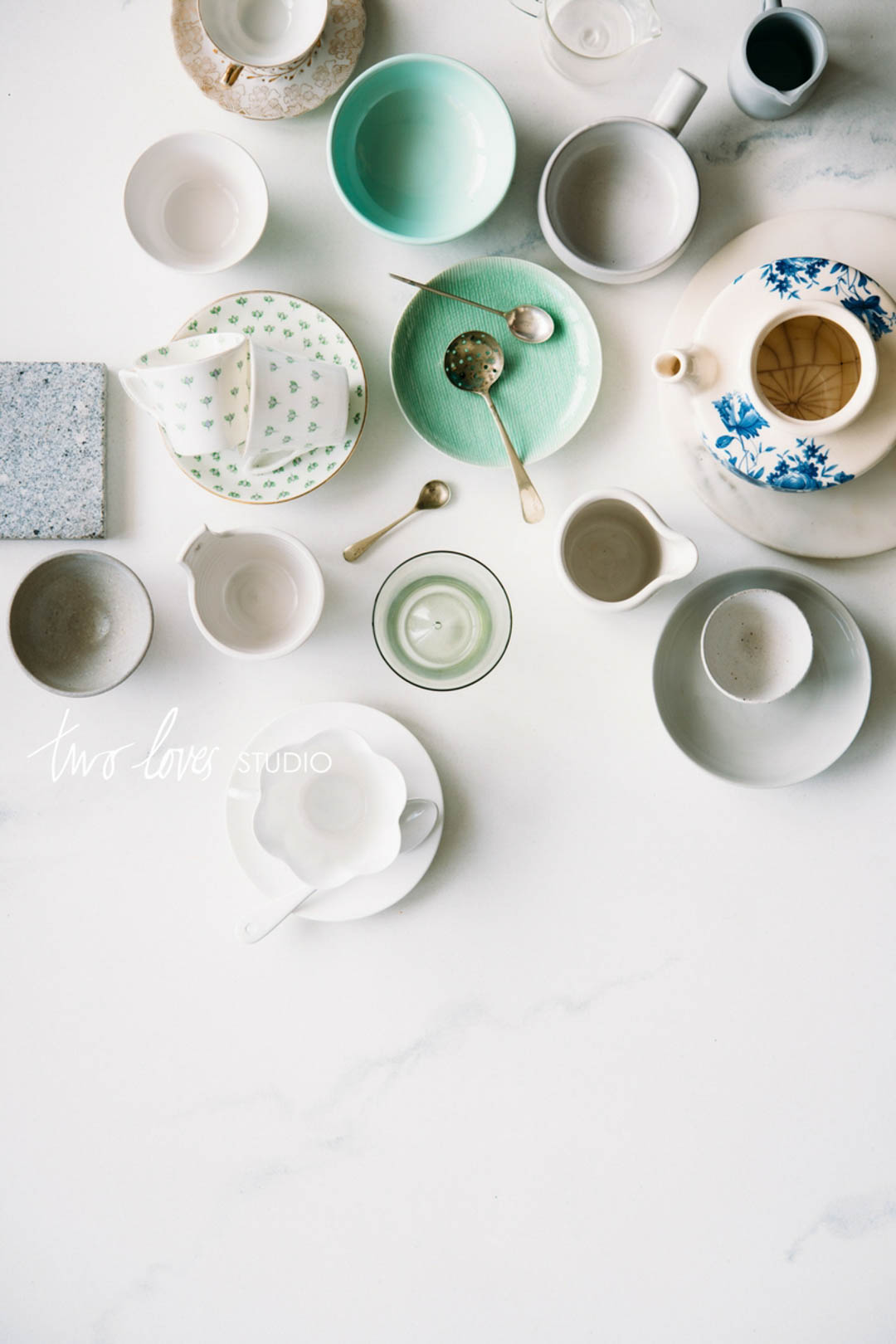 An assortment of tea cups, plates and spoons on a white backdrop.