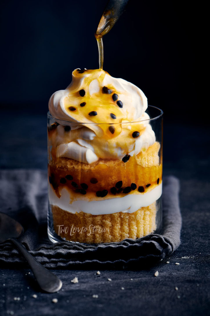 Dark blue linen background with a clear glass and a passionfruit layered dessert. 