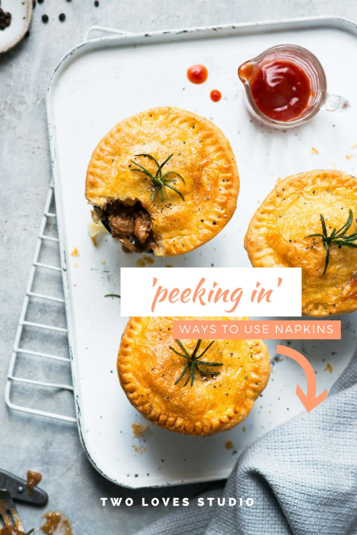 Example in composition for food photography showing a soft blue background with a cooking tray set with three meat pies and a linen napkin poking in frame on bottom right corner. 