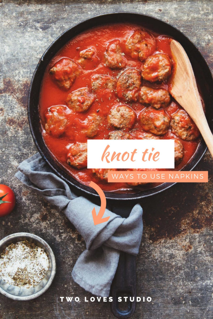 Marble background with a cast iron pan, red sauce and meat balls. A light blue linen napkin tied to the handle. 