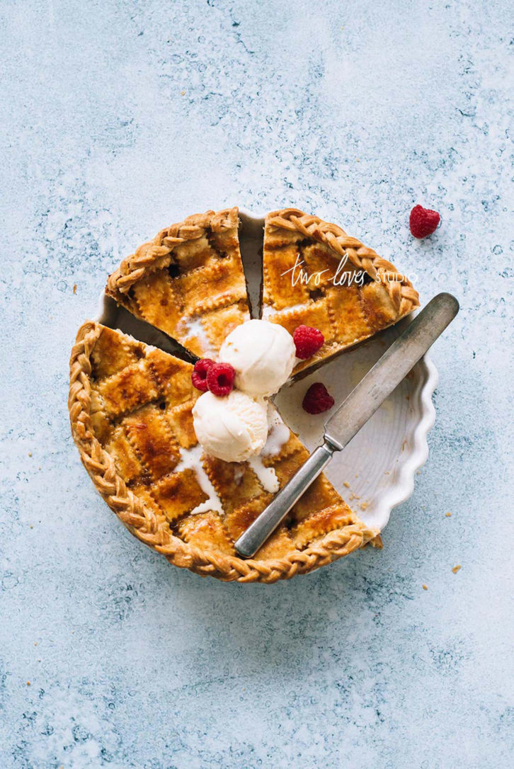 An apricot pie with a lattice and a braid around the edges. Topped with two scoops of ice cream and raspberries.