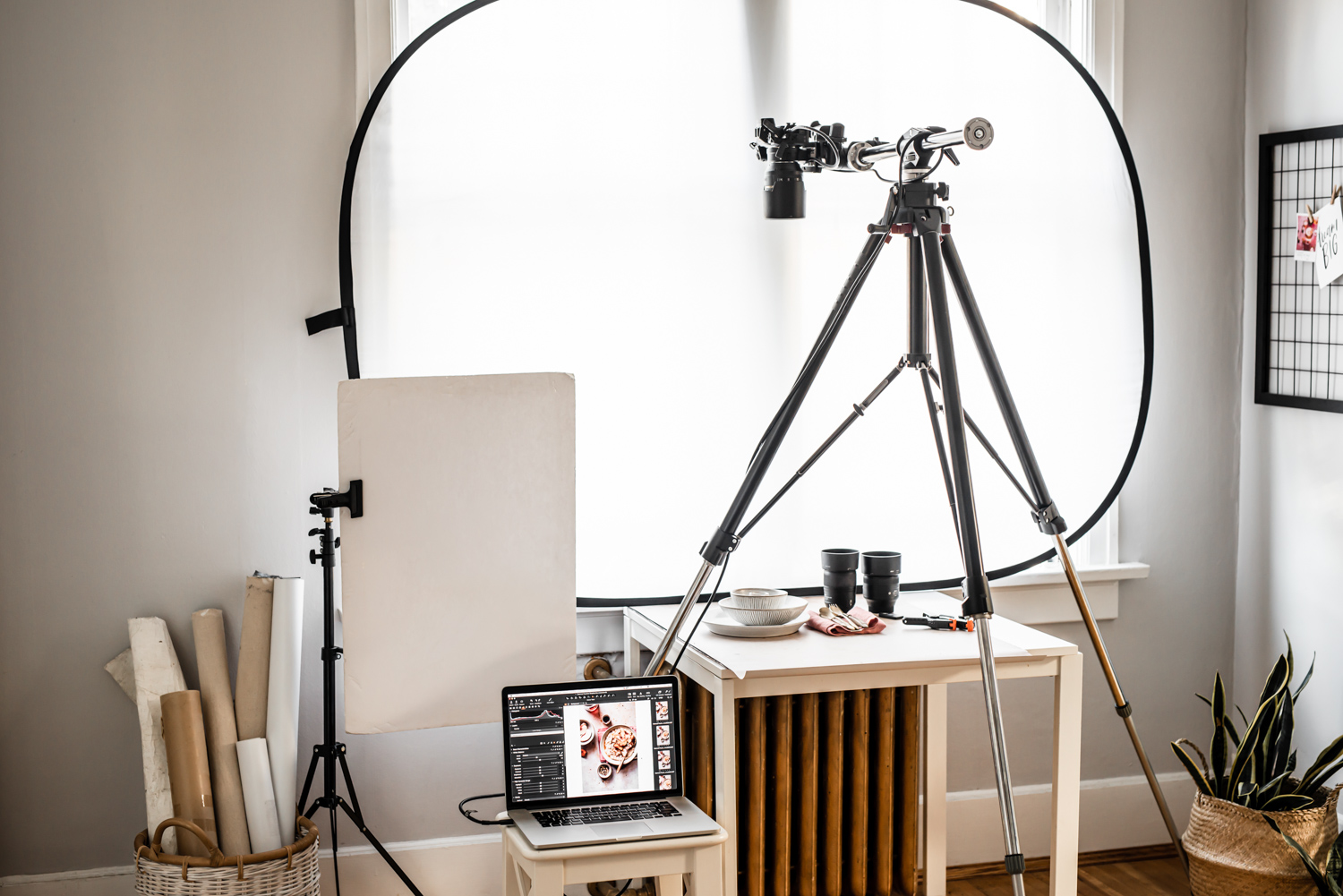 Basic food photography equipment set up. A vinyl backdrop, trip over a white square table with foam boards and lenses. 