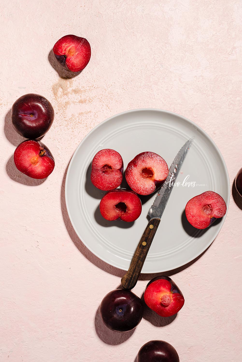White plate with a knife and sliced plums. 