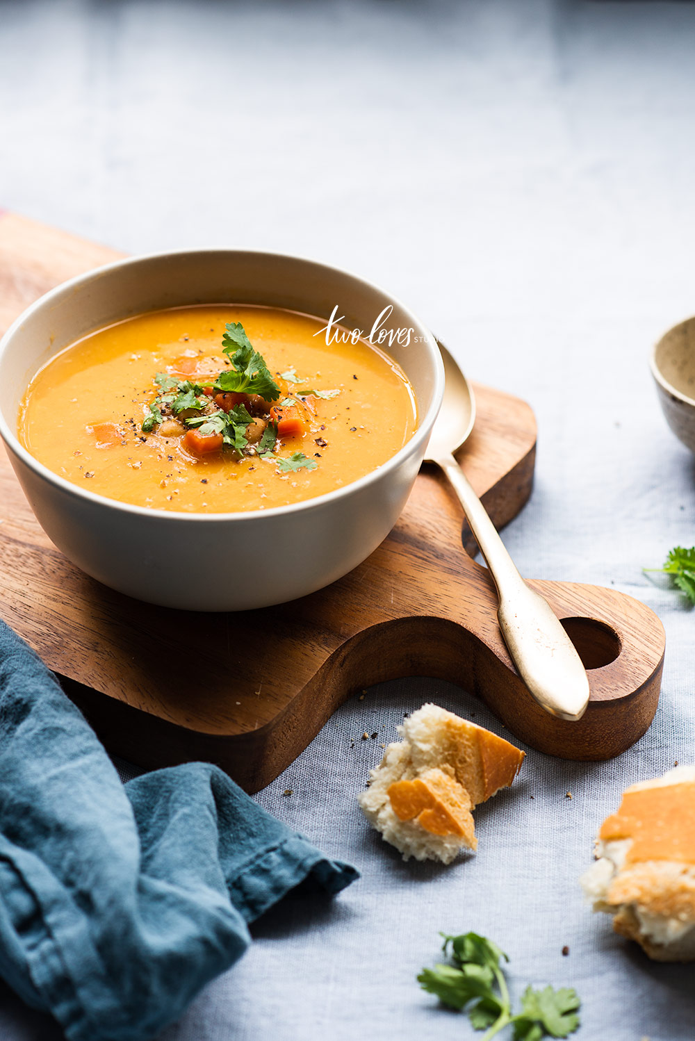 A bowl on a wooden boat full of soup and pieces of bread around the setting. 