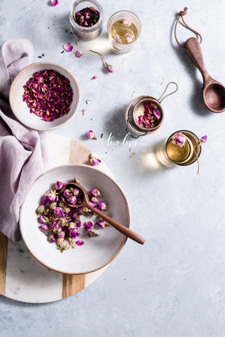 Dry rose buds and petals in a bowl, with rose tea on the side.