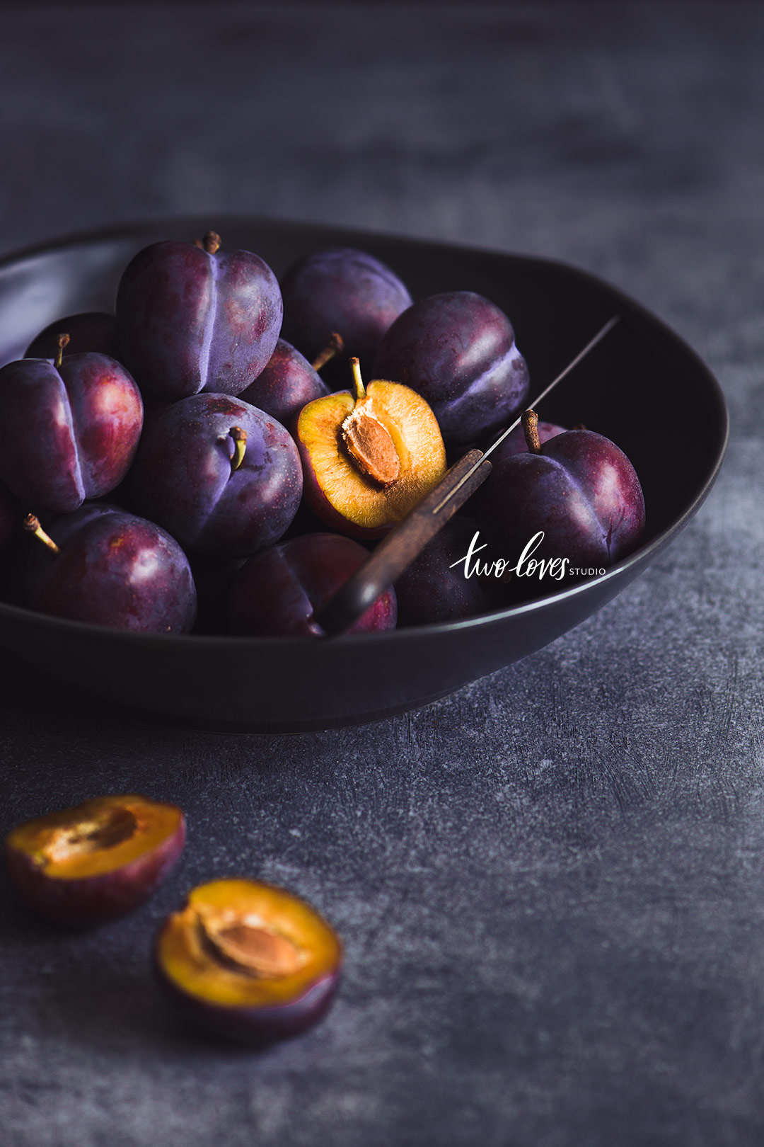 A bowl of plums and one cut in half