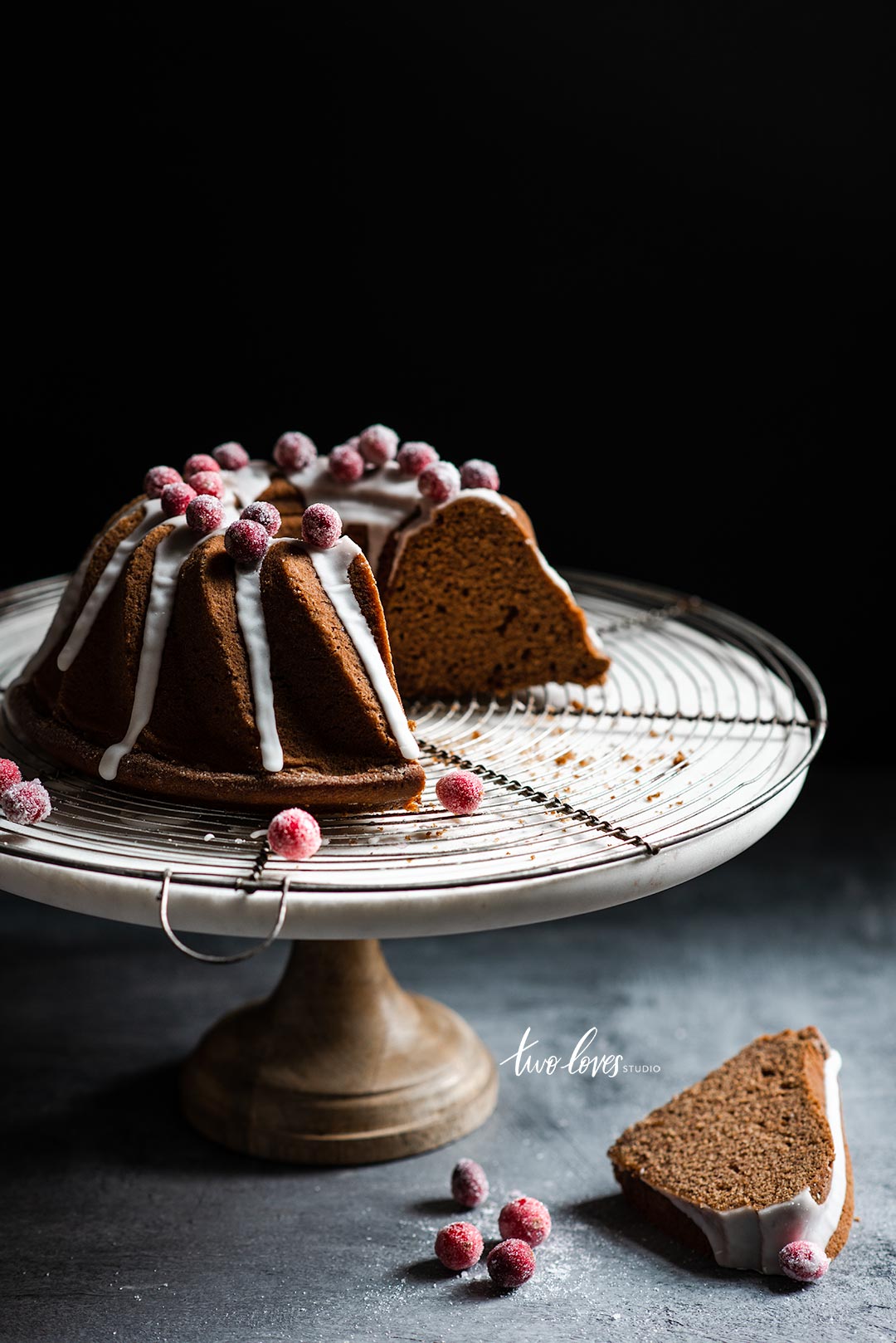 Bundt cake with a white frosting and frosted berries on a cake stand a wire cooling rack. 