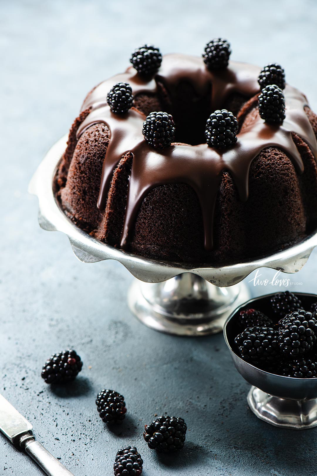 A chocolate bundt cake with chocolate frosting and blackberries scattered out the cake. 