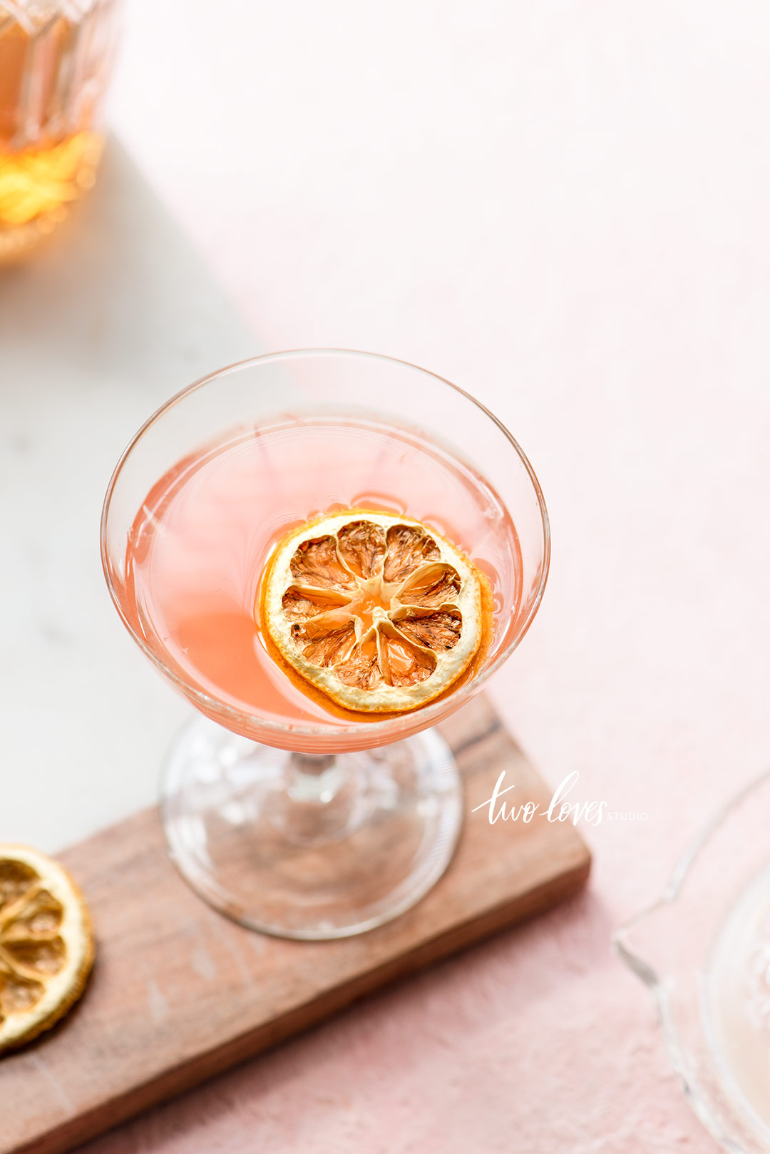 A pink cocktail glass on a wooden board with a dried slice of fruit in the glass. 