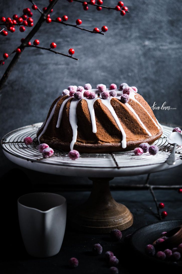 Bundt cake on a cake stand with a wire cooling rack. White frosting and frosted berries. 