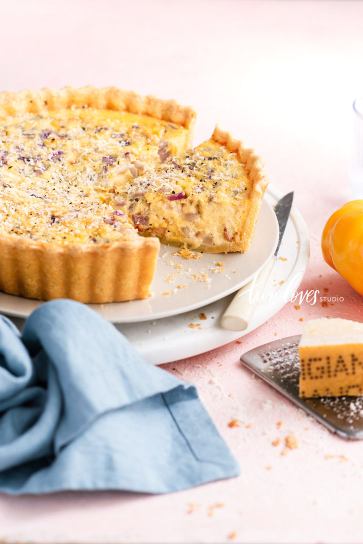 Bacon, onion quiche cut into a slice with a blue napkin. 