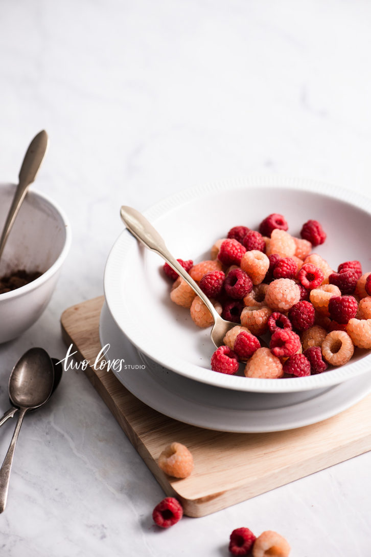A bowl of raspberries, red and yellow showing the light coming from the right side of the bowl. 