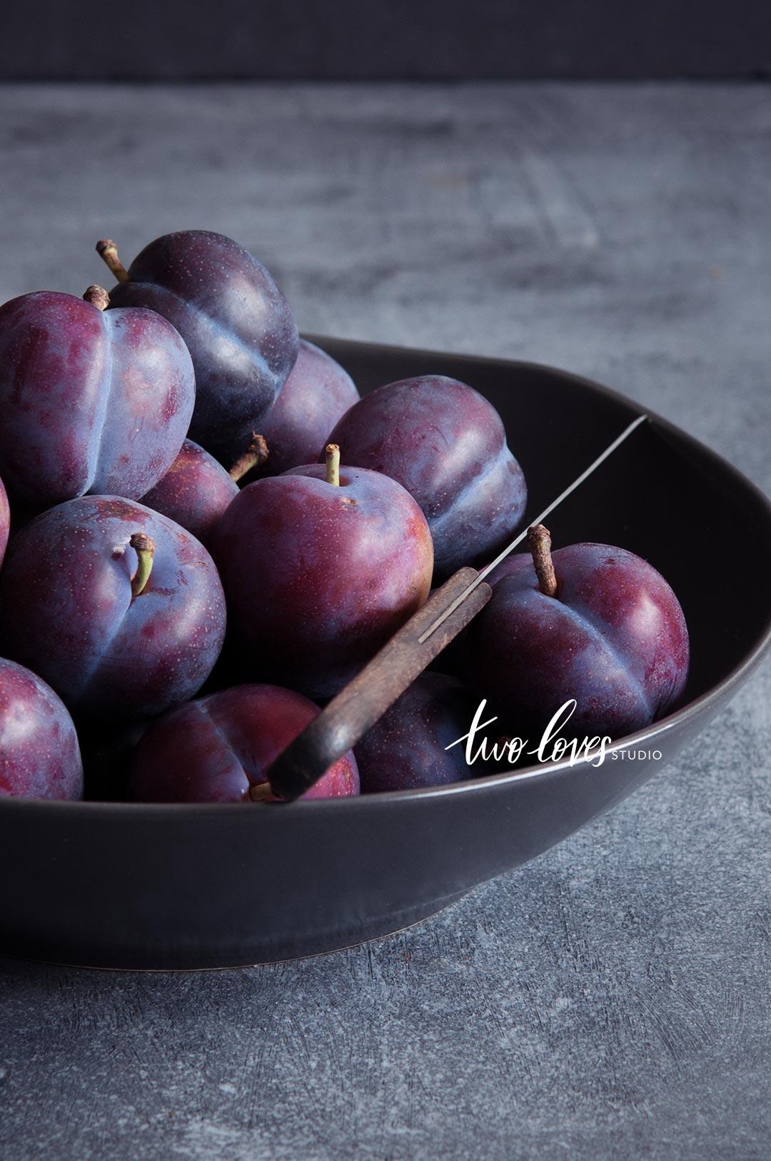 A bowl of plums in a dark lighting setup.