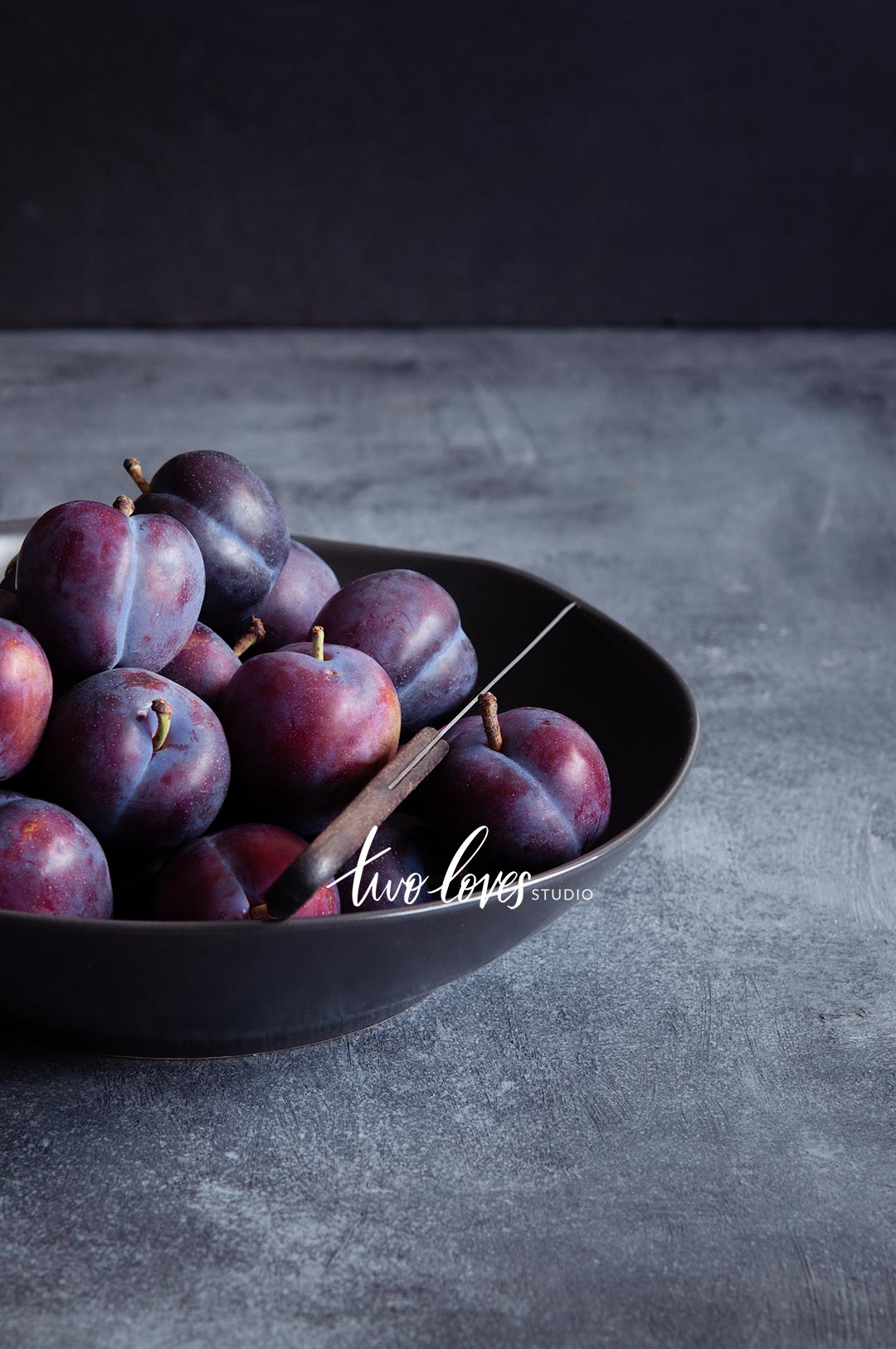 A bowl of plums in a dark lighting setup.