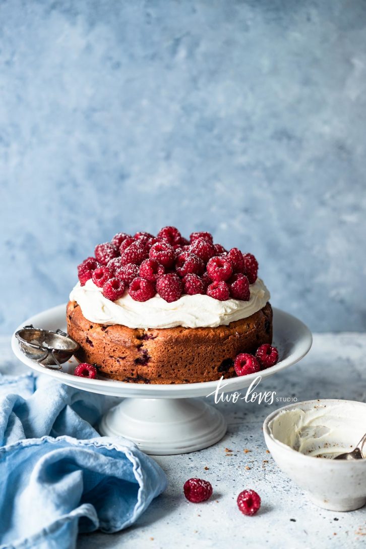 Cake stand with a circle cake cream cheese frosting a raspberry topping.