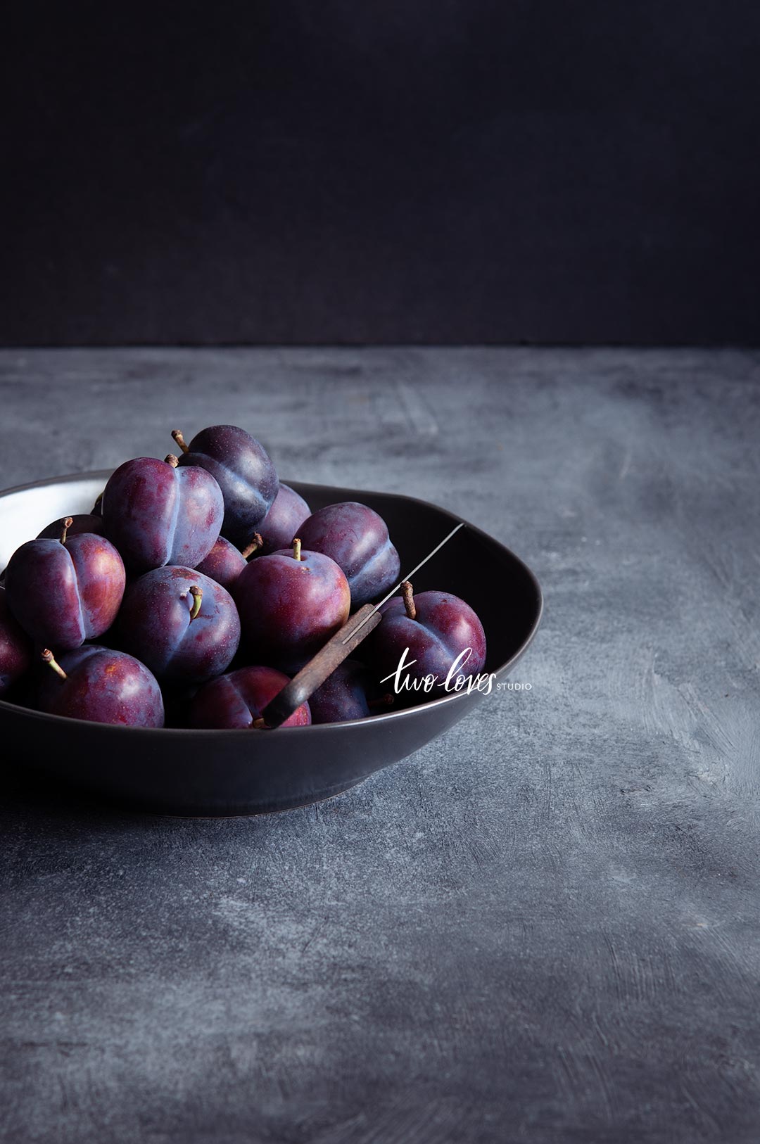 A bowl of plums in a dark lighting setup.