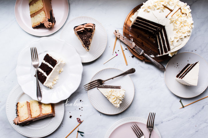 Large white and chocolate layered cake on a white marble background with an assortment of slices cut from the cake.