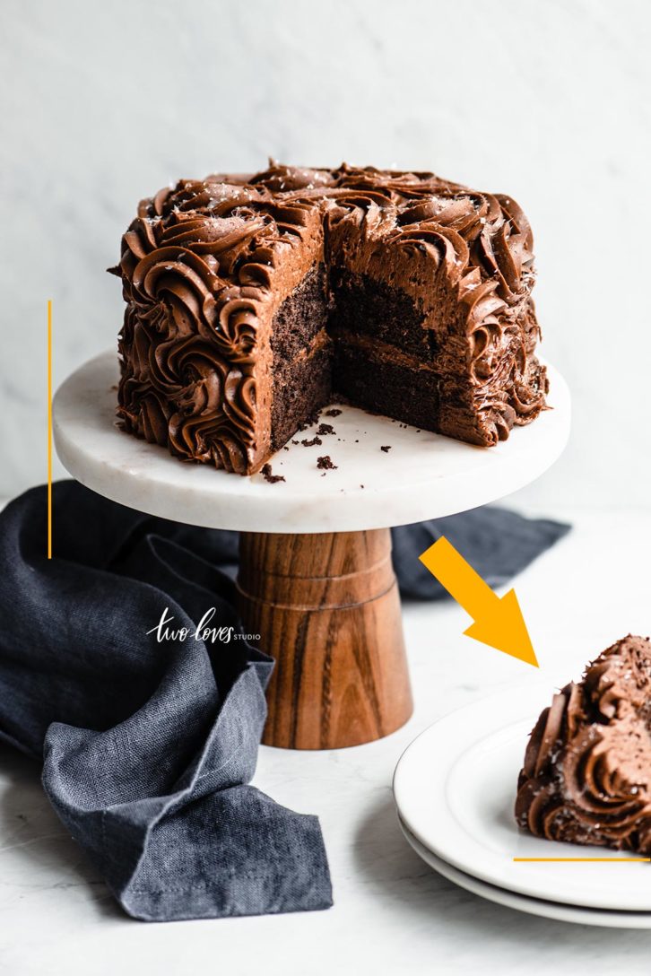 Chocolate cake on top of a cake stand with a slice cut out on a white background.