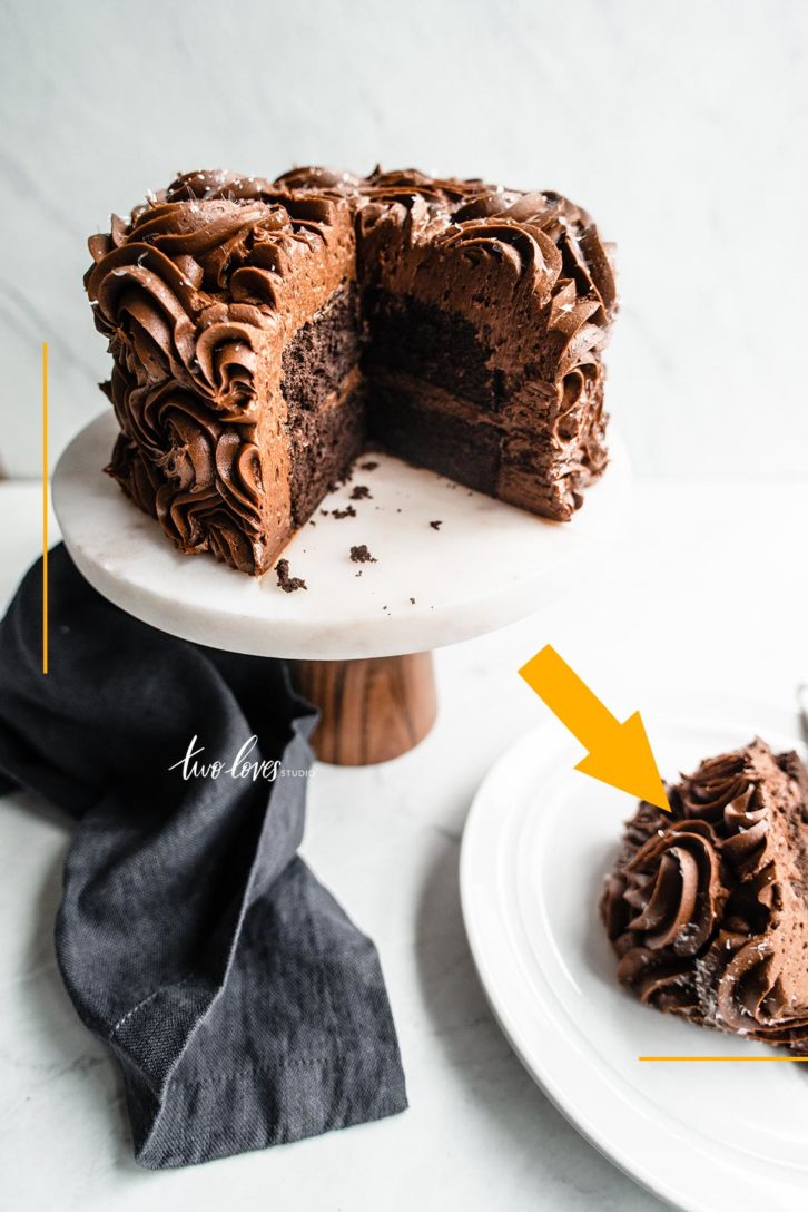 Chocolate cake on top of a cake stand with a slice cut out on a white background.