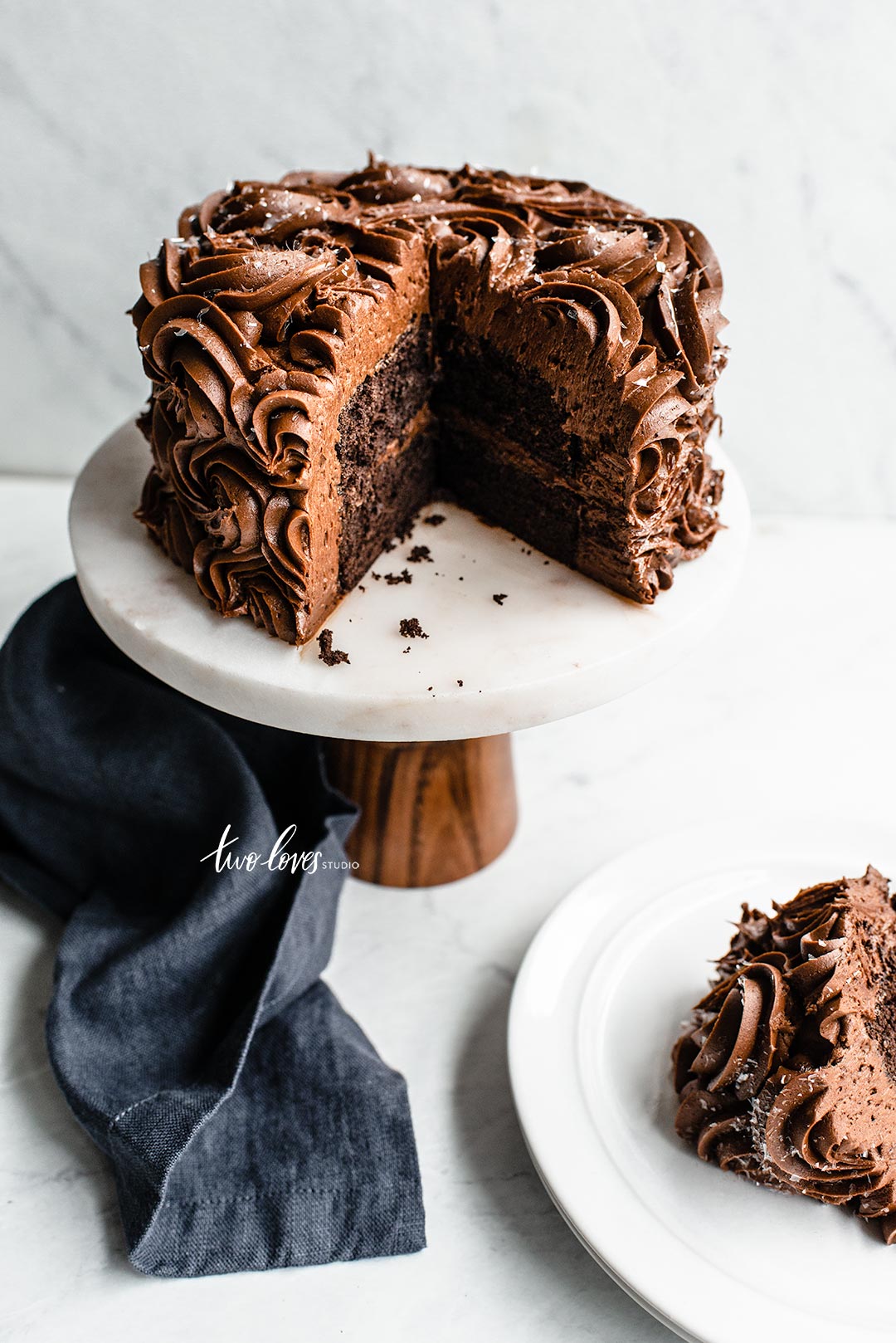 Chocolate cake on a white cake stand with a blue napkin showing a wide lens distortion.