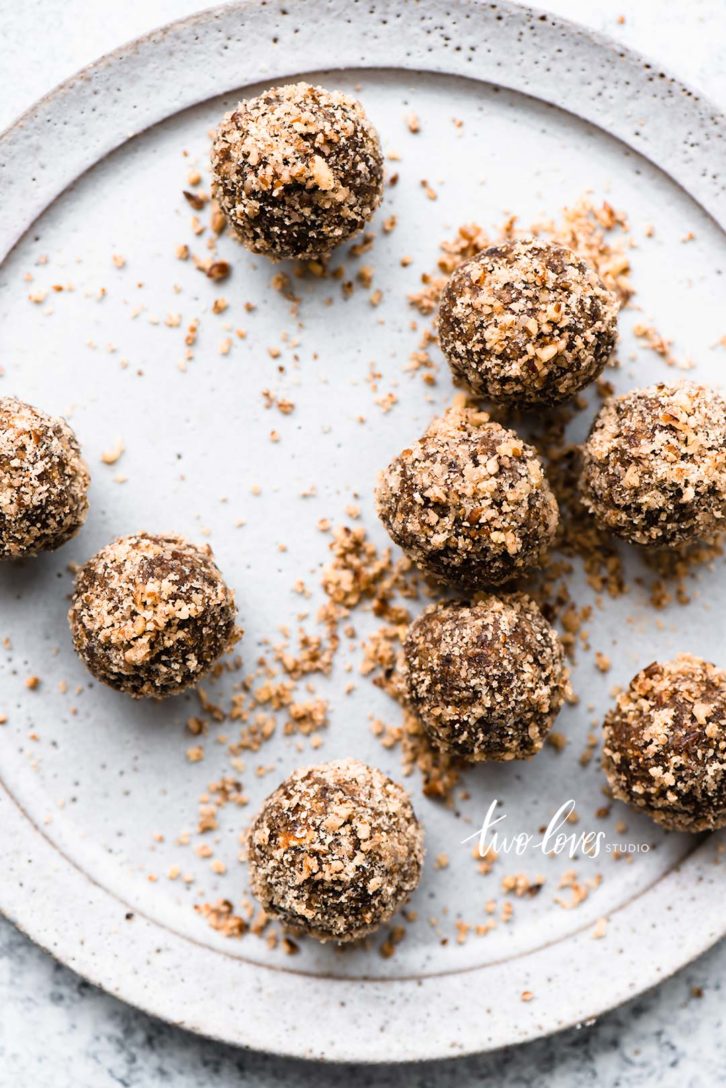 A white plate of round chocolate protein bites with nuts on top.