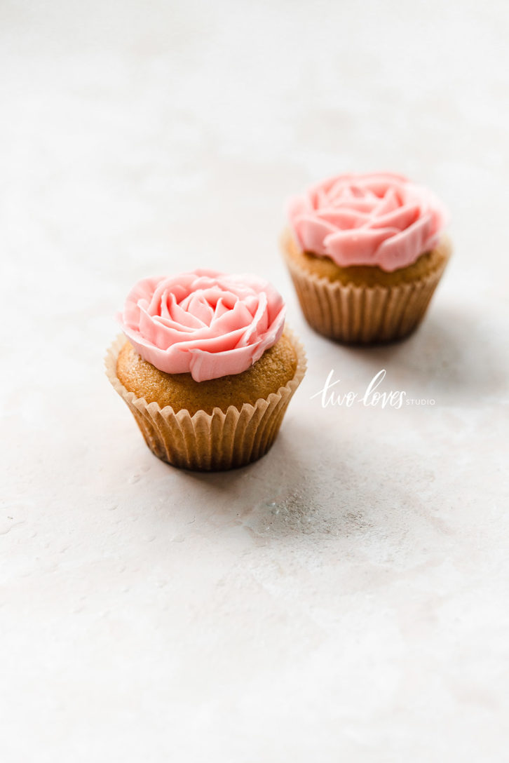 Two cupcakes with pink flowers piped on top.