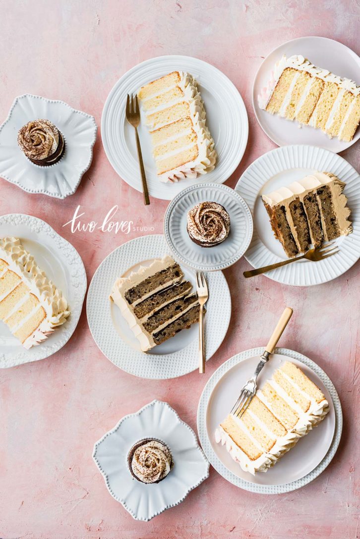 Plates of a white layered cake and cupcakes with plates and forks. 