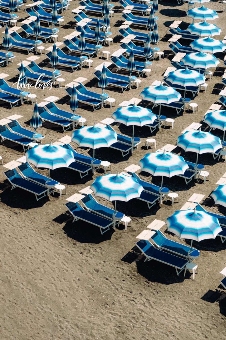 rows of blue striped umbrellas on the beach in italy.