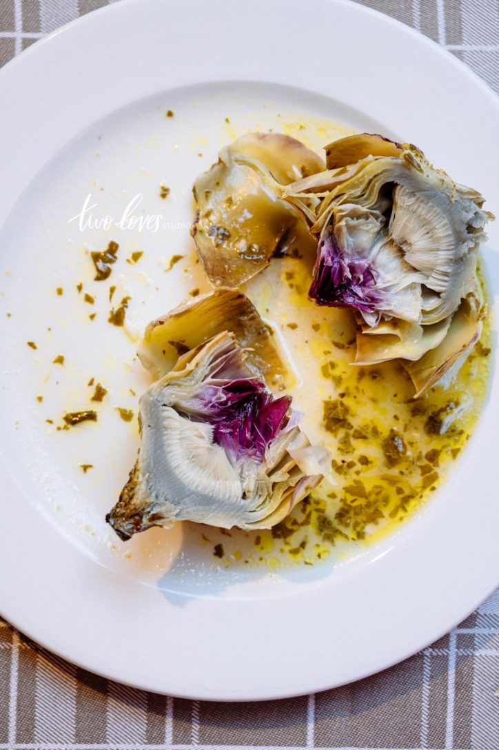 A white plate with a cut up artichoke in the centre of the plate.