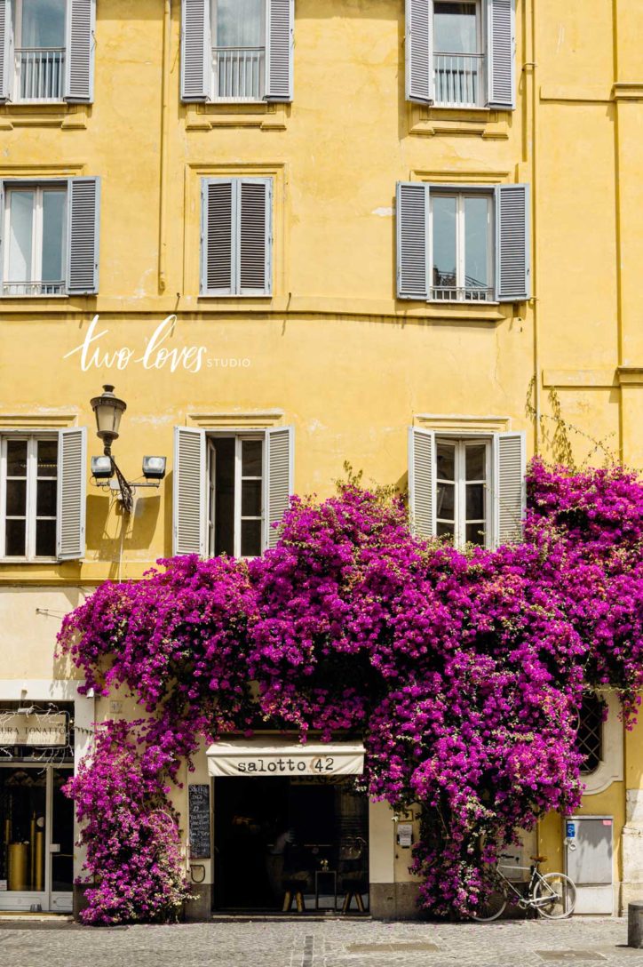 A yellow building in Italy with purple flowers framing the doorway.