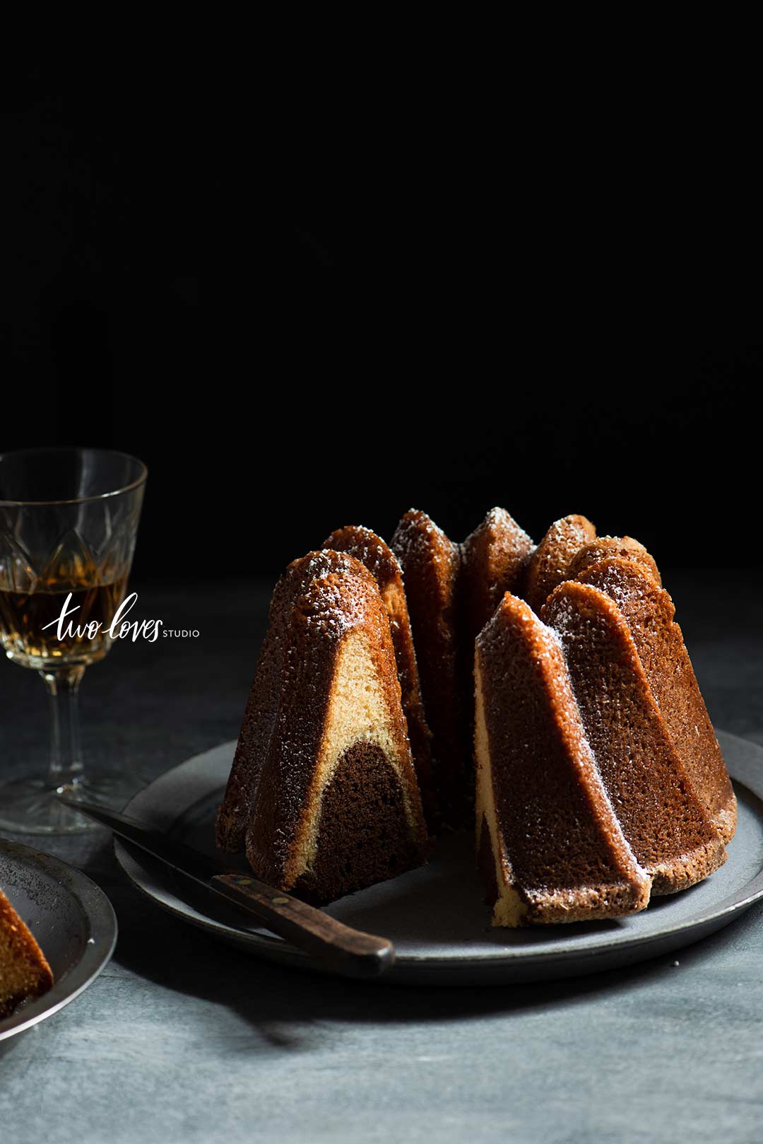 Low light food photography with bundt cake on plate and glass of brandy.