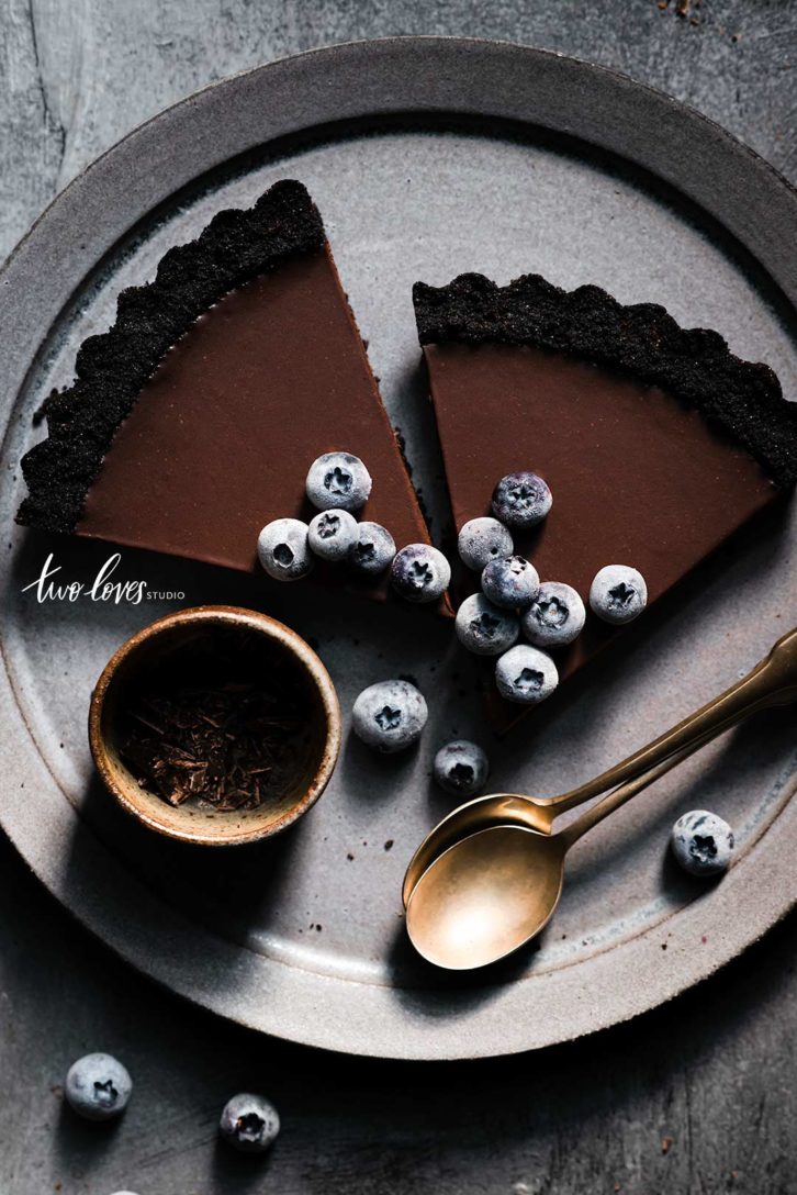 Low light food photography overhead of a chocolate Oreo tart with frozen blueberries.