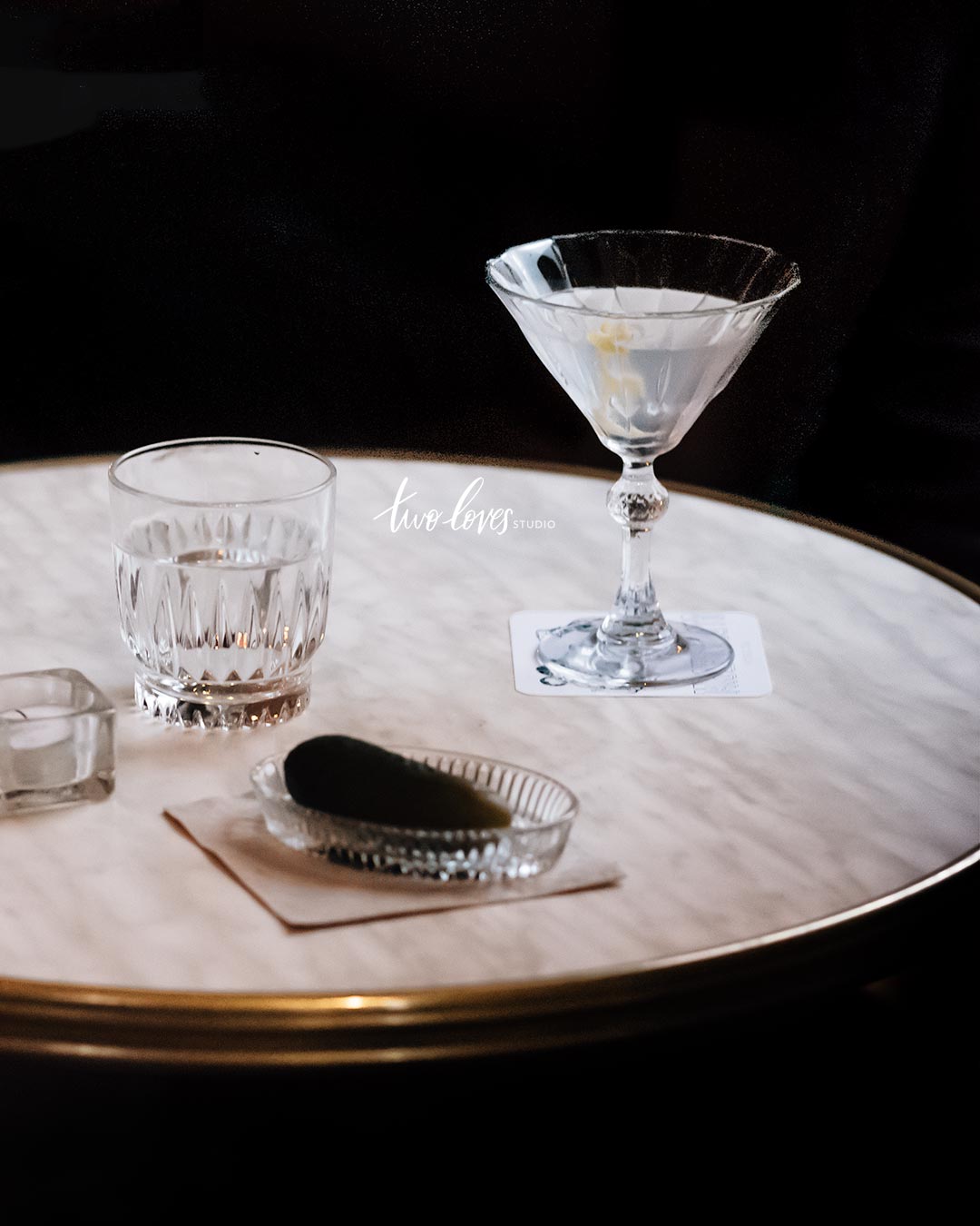 Side table with a martini cocktail, side of water and a pickle.  