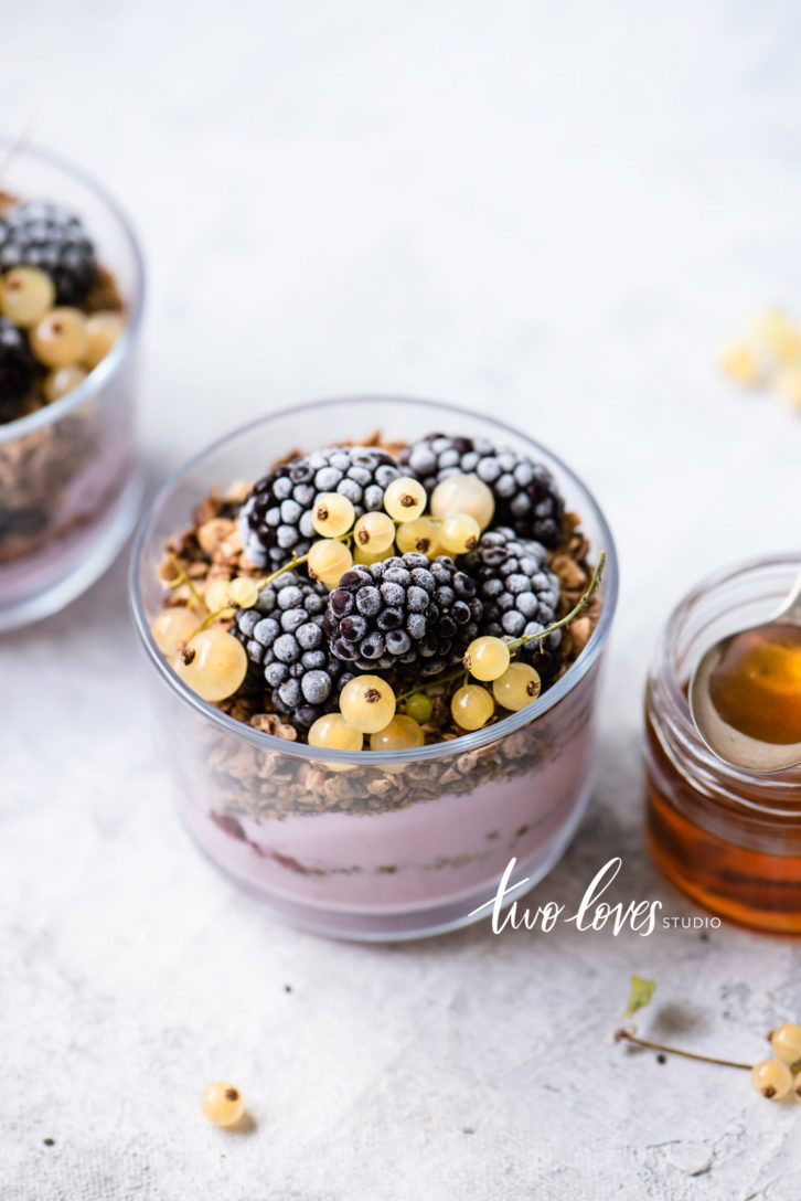 Blackberry granola yoghurt with white currents in a dish, with a side of honey.