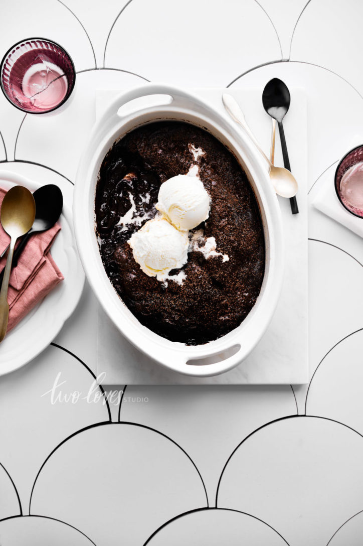 overhead shot of chocolate cobbler in a white dish with two scoops of ice cream.