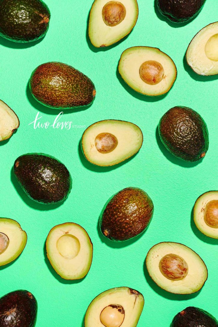 Flat-lay of avocados, some cut open others whole. 