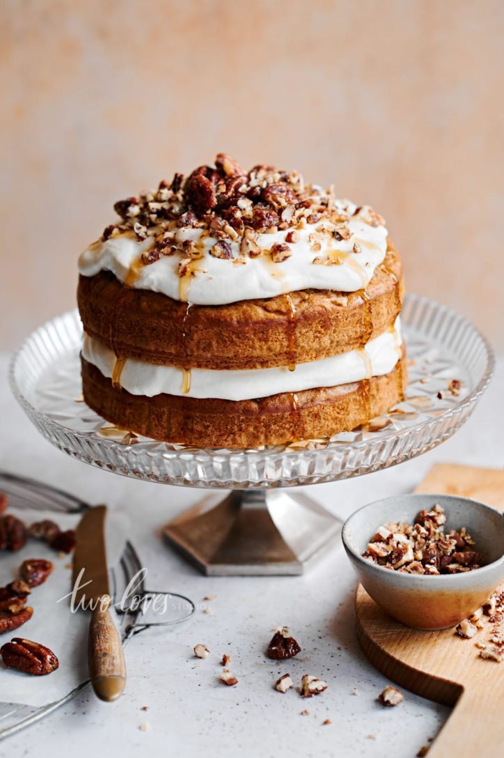 Layered carrot cake with cream cheese icing and maple syrup drizzle. Topped with chopped pecans.