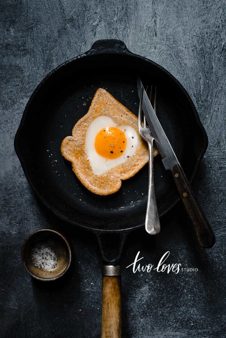 A slice of bread with a heart shaped egg in the middle. Sitting in a black skillet.