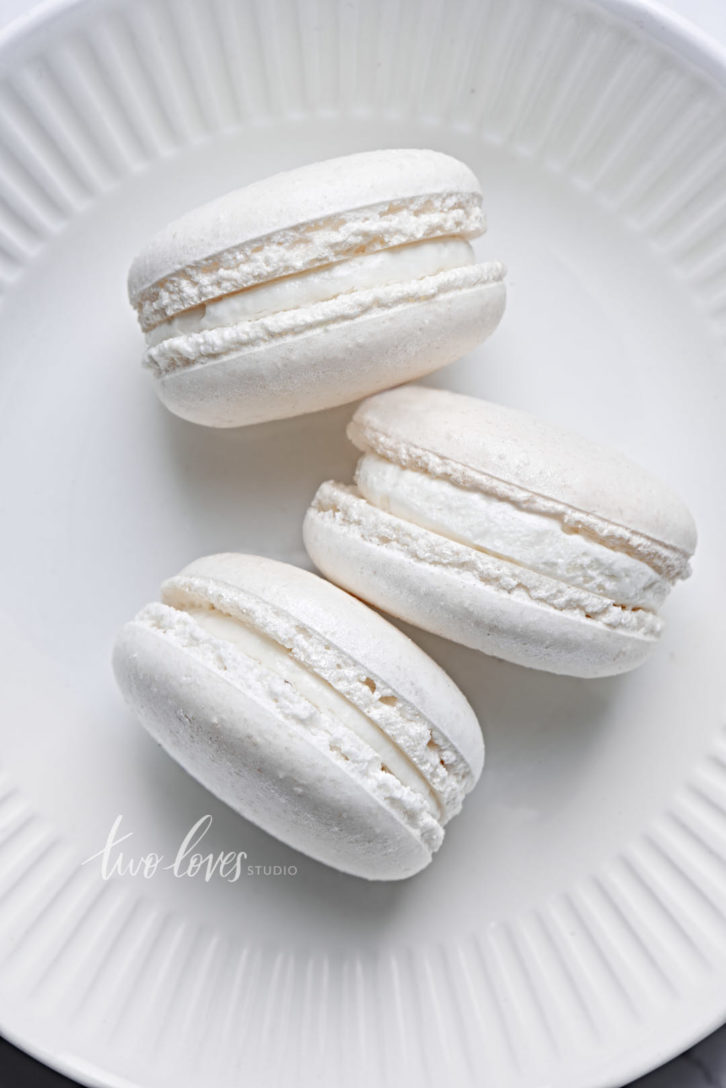 Three white macarons on a plate.