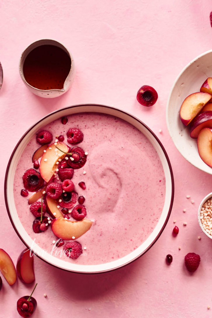 Overhead shot of a pink smoothie bowl topped with summer fruit. The photos uses analogous colours, of pink, orange and red. Colours that are next to each other on the colour wheel.