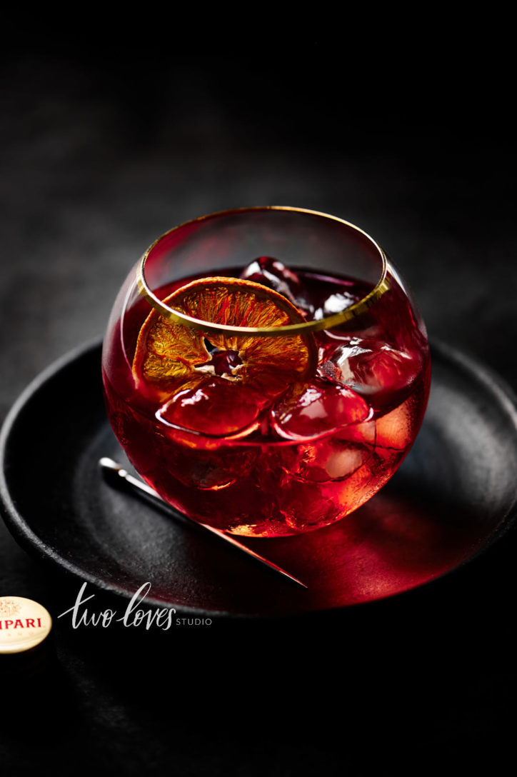A dark portrait of a Negroni with a slice of dehydrated orange. Showing camera settings for food photography for shallow depth of field.