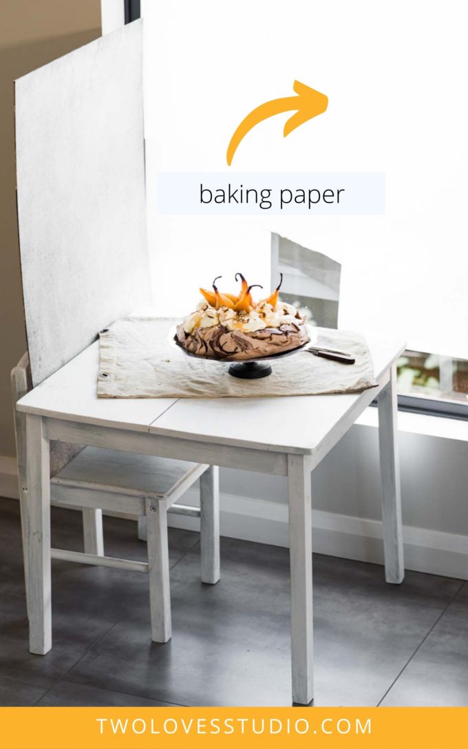 Pavlova sitting on a small children's table next to a window. Showing natural light food photography set up.