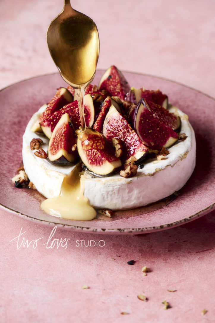 A wheel of brie cheese with slices fig on top drizzled in honey. 