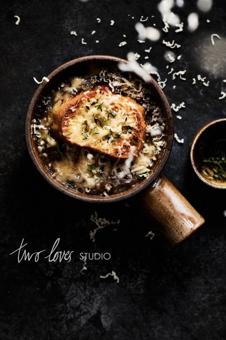 An overhead photo of french onion soup with grated cheese falling from above. Showing camera settings for food photography and freezing motion.