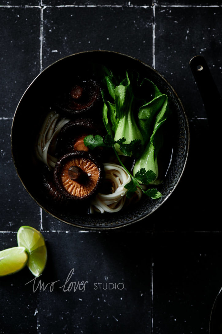 Black background with a black bowl with ramen inside and slices of lime