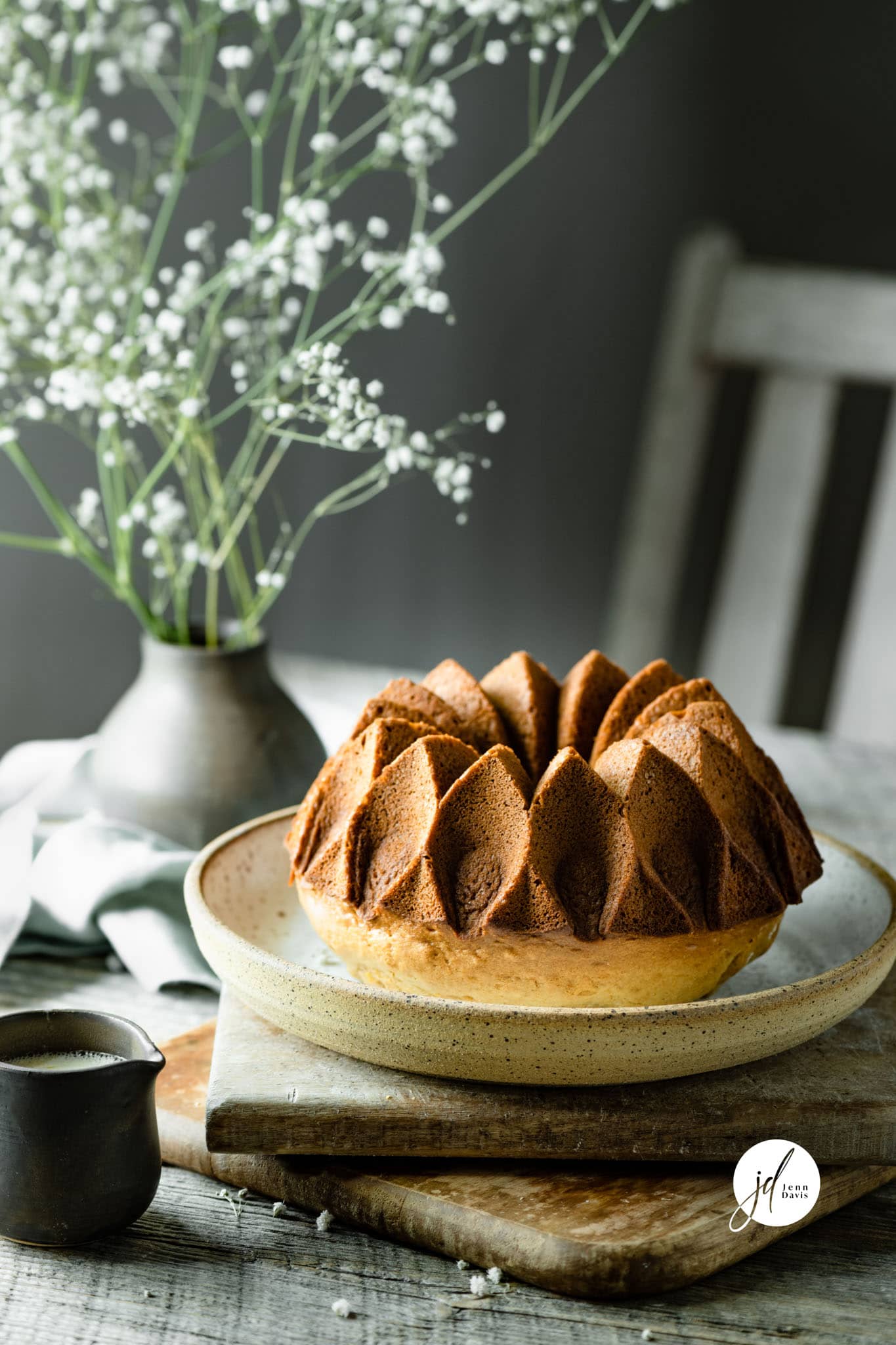 Bunt Cake on a dish with a table setting of baby breath flowers in the background. This was shot by Jenn Davis using her favourite food photography lens. AF-S Micro Nikkor.