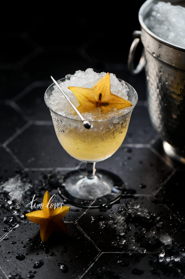 Black Hexagon tile backdrop with crushed ice and  star fruit in a cocktail glass. 