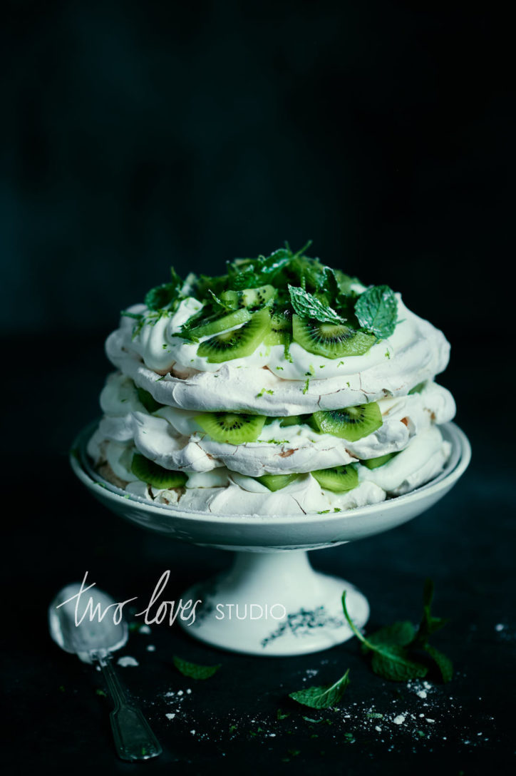 Kiwi layered pavlova on a black background, shot taken with Rachel Korineks favourite food photography lens Nikkor AF-S 85mm.