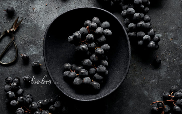 Black grapes in a black bowl on on black flat-lay.